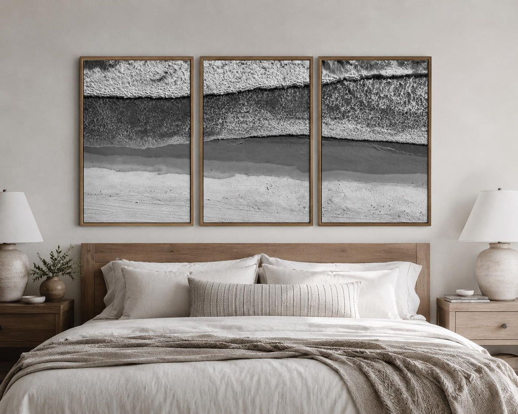 May include: A triptych of three rectangular wall art prints featuring a black and white aerial view of ocean waves crashing onto a sandy beach. Each print is encased in a thin, light-toned wooden frame, displayed side by side on a wall.