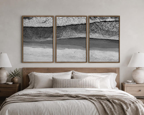 May include: A triptych of three rectangular wall art prints featuring a black and white aerial view of ocean waves crashing onto a sandy beach. Each print is encased in a thin, light-toned wooden frame, displayed side by side on a wall.