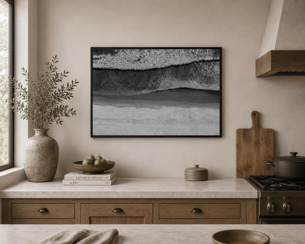 May include: A rectangular wall art print in a black frame featuring an aerial black and white photograph of ocean waves crashing onto a sandy beach. The image displays horizontal bands of white sea foam, dark water, and light-toned sand textures.