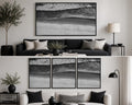 May include: A black and white aerial photograph of a shoreline with crashing waves, sand, and water. The artwork is presented as a single large horizontal framed print or as a set of three vertical framed prints, both featuring the same coastal scene.