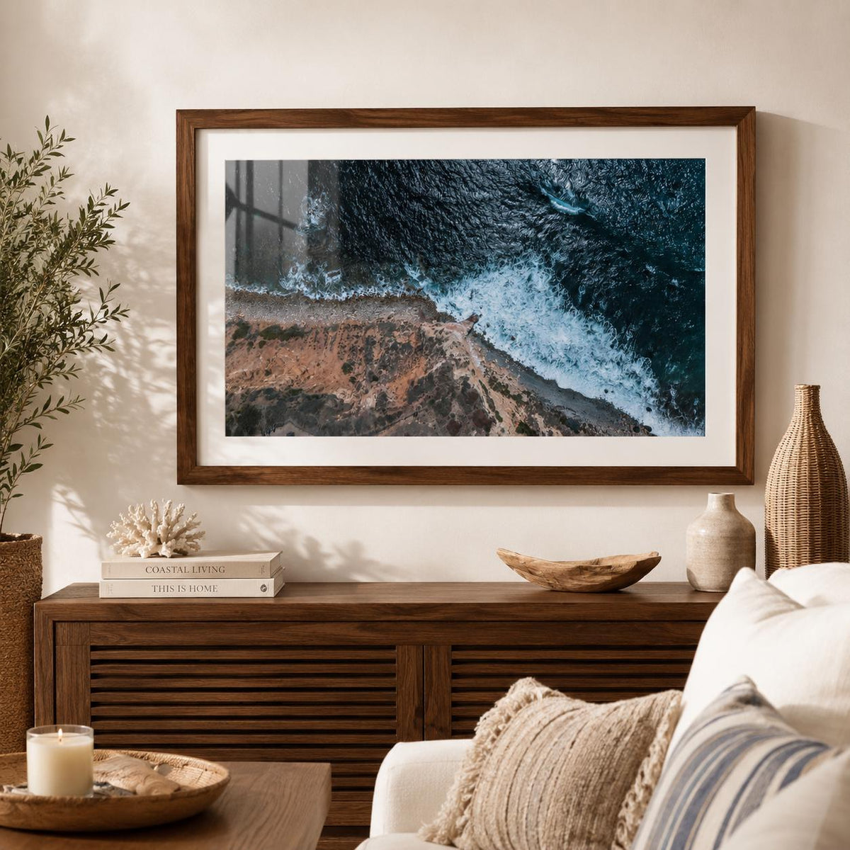 May include: A framed landscape photograph featuring an aerial view of a rugged coastline where dark blue ocean waves crash against a rocky, tan-colored shore. The artwork is enclosed in a dark brown wooden frame with a wide white mat border.