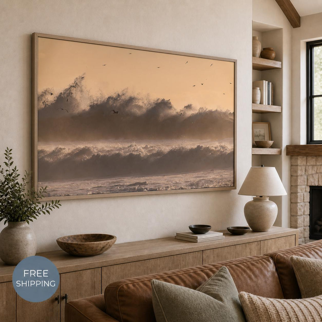 May include: A large rectangular framed wall art print depicting a turbulent ocean scene with crashing waves and birds in flight against a soft peach-toned sky. The artwork is displayed in a light-colored wooden frame on a neutral wall.