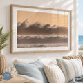 May include: A rectangular framed wall art print featuring a sepia-toned ocean scene with large crashing waves and a hazy, light orange sky. The artwork is enclosed in a light-colored wooden frame with a wide white mat border surrounding the image.