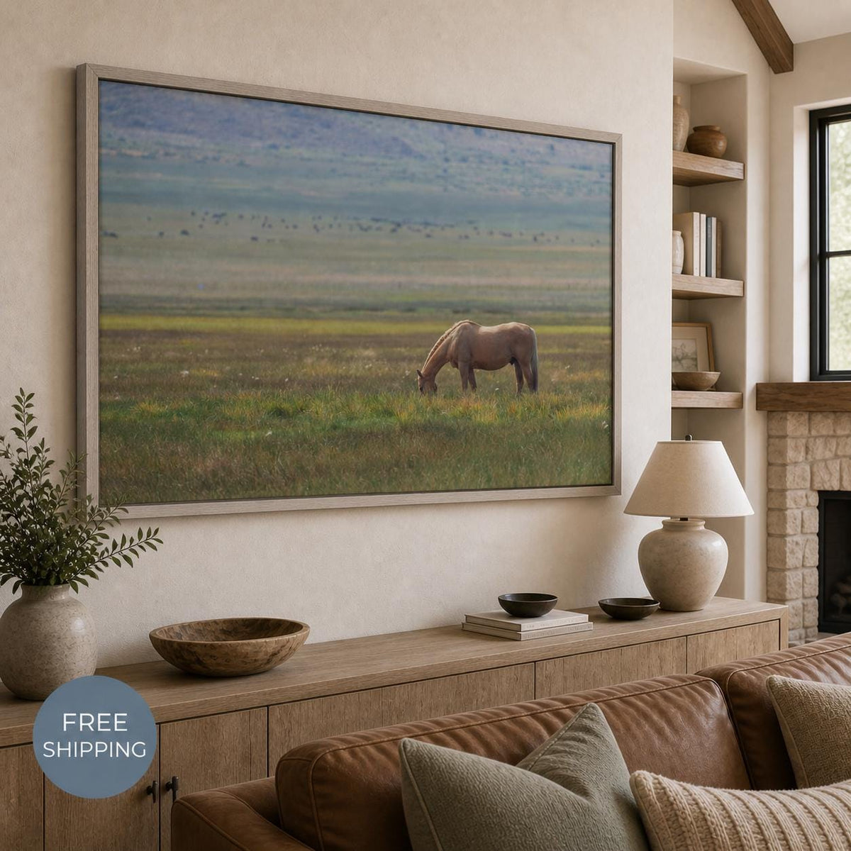 May include: A rectangular wall art print featuring a light brown horse grazing in a vast, grassy field under a soft, overcast sky. The artwork is framed in a light-toned wood border and displayed above a wooden console table in a living space.