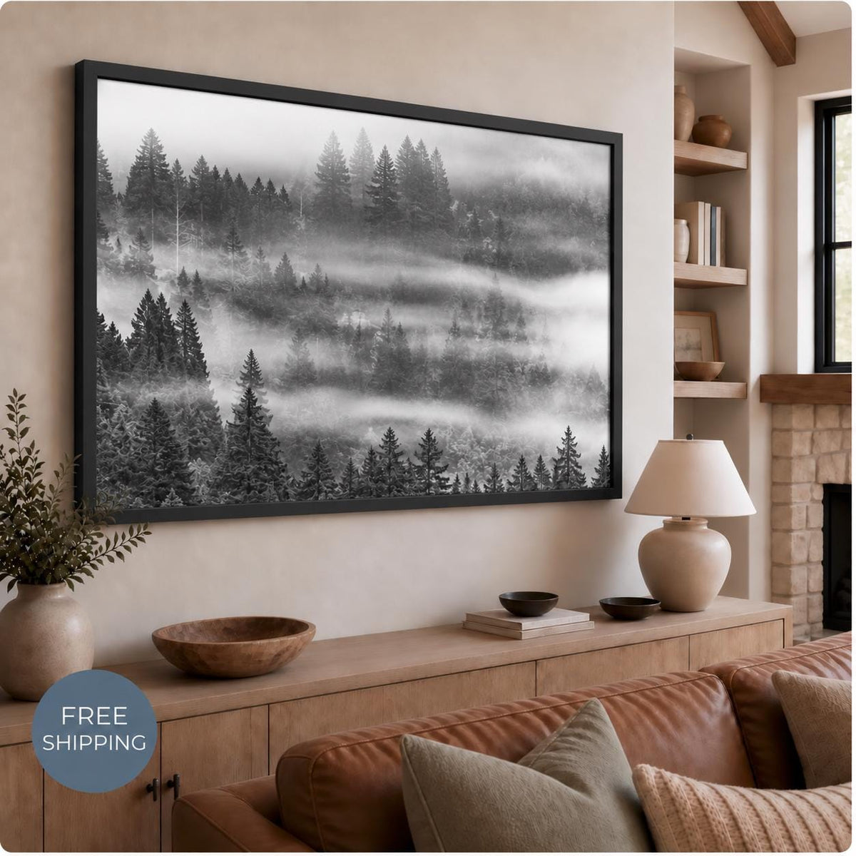 Misty forest canvas in a Black Matte floating frame above a wooden console and brown sofa. Black evergreen silhouettes contrast with white and gray fog. A badge reads Free Shipping.