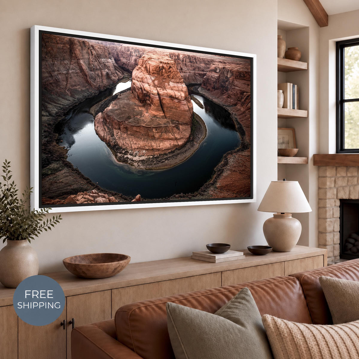 White floating frame surrounding a Horseshoe Bend canvas print, with a visible shadow gap. Warm canyon cliffs and the blue-green river hang above a light wood sideboard with pottery and a lamp. Free Shipping badge at lower left.