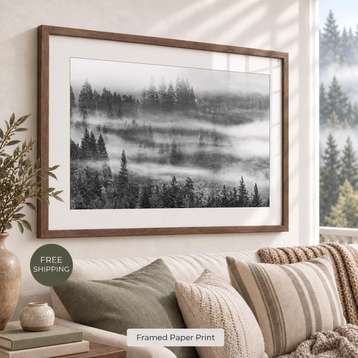 Misty evergreen forest photograph in black and white, with a white mat and warm brown Walnut Flair frame, displayed above a neutral sofa. Room mockup for the walnut finish.